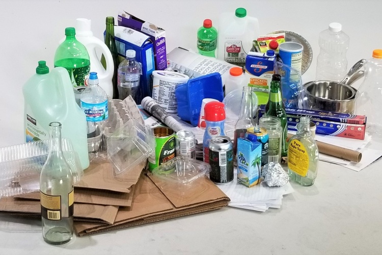 Photo of mixed recyclables. Plastic bottles, flattened cardboard, metal cans, glass bottles, and other good recyclables.